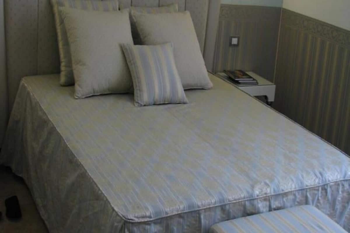 A neatly made bed with a striped bedspread and two pillows, a bedside table with a book, and a wall with vertical paneling.
