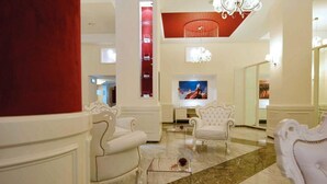 Un vestíbulo amplio con mobiliario blanco, una gran pantalla de televisión y una pared decorativa roja.
