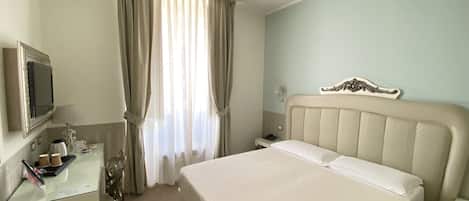 A hotel room with a bed, a desk with a television, and a window with curtains.