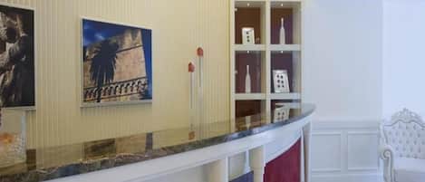 A reception area with a marble counter, a framed picture, and a white chair.