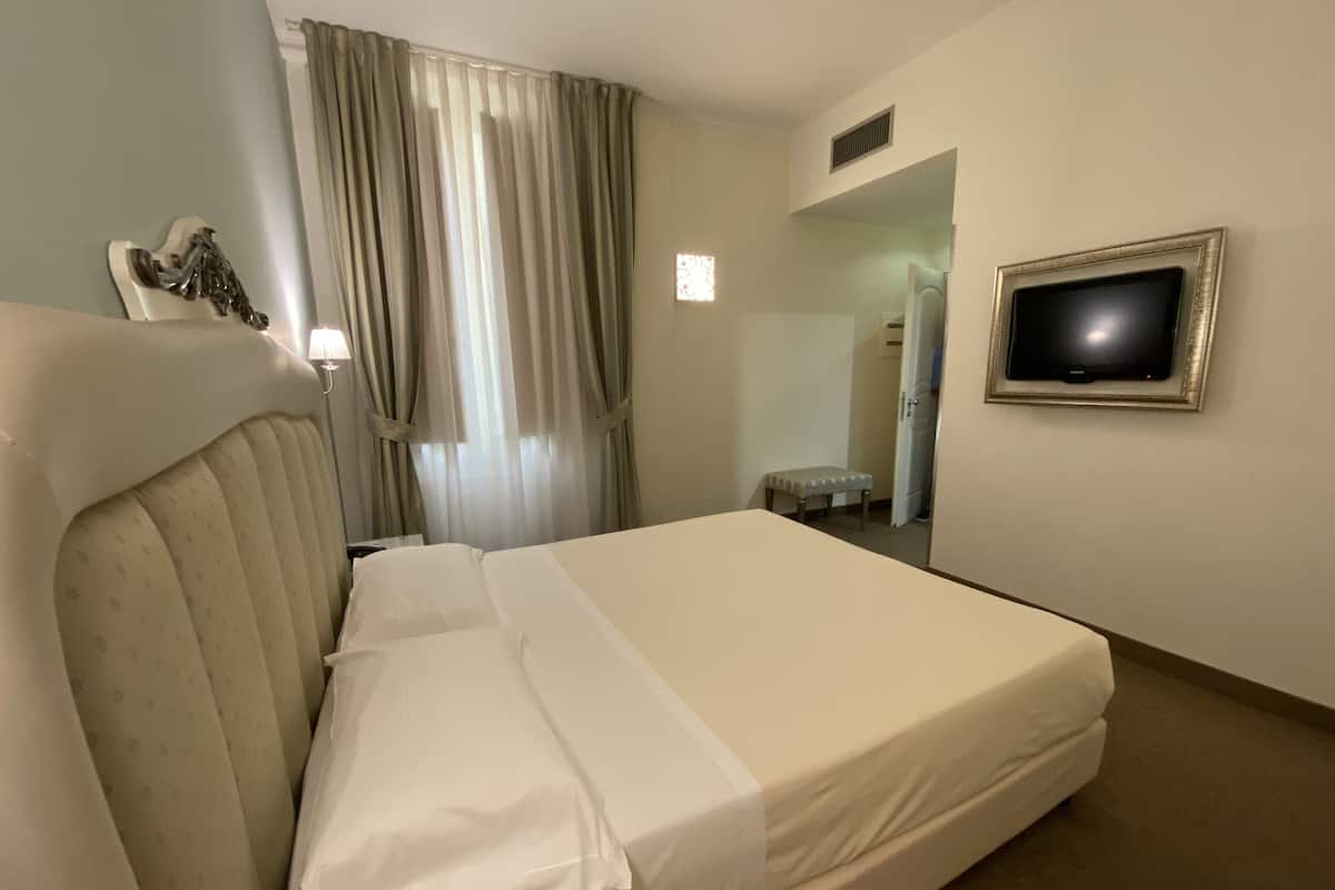 A hotel room with a bed, curtains, a television, and a bench.