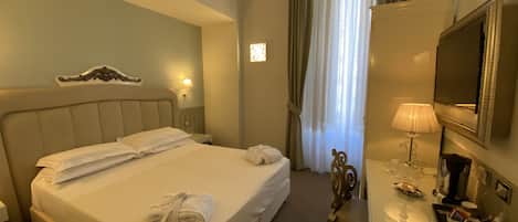 A hotel room with a large bed, a desk with a lamp, a TV, and a window with curtains.