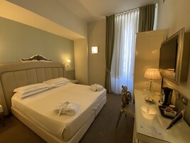 Ein Hotelzimmer mit einem großen Bett, einem Schreibtisch mit Lampe, einem Fernseher und einem Fenster mit Vorhängen.
