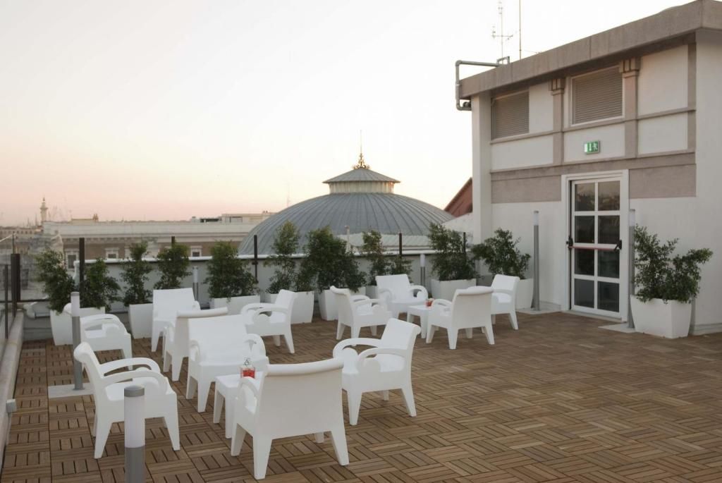 A rooftop terrace with white plastic chairs and tables, a large dome structure, and a building with an exit sign.