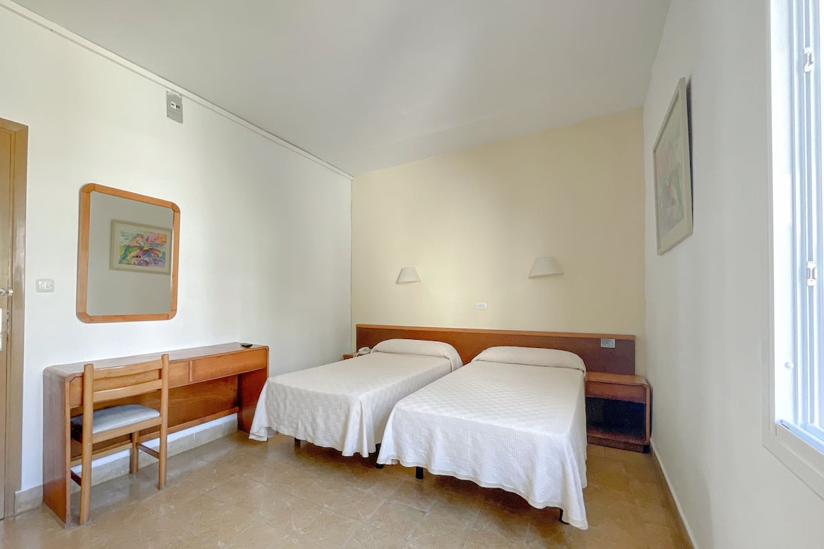A hotel room with two single beds, a wooden desk, and a chair.