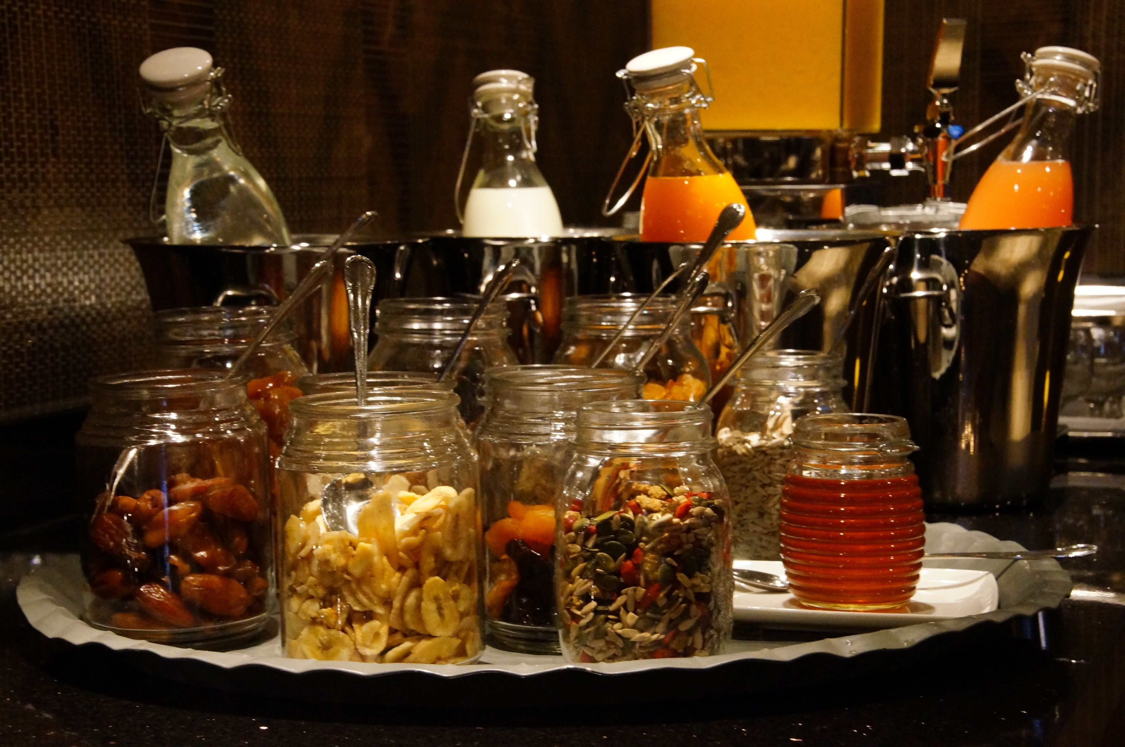 Una bandeja con diversos alimentos y bebidas, incluyendo tarros de nueces, frutas secas y miel.