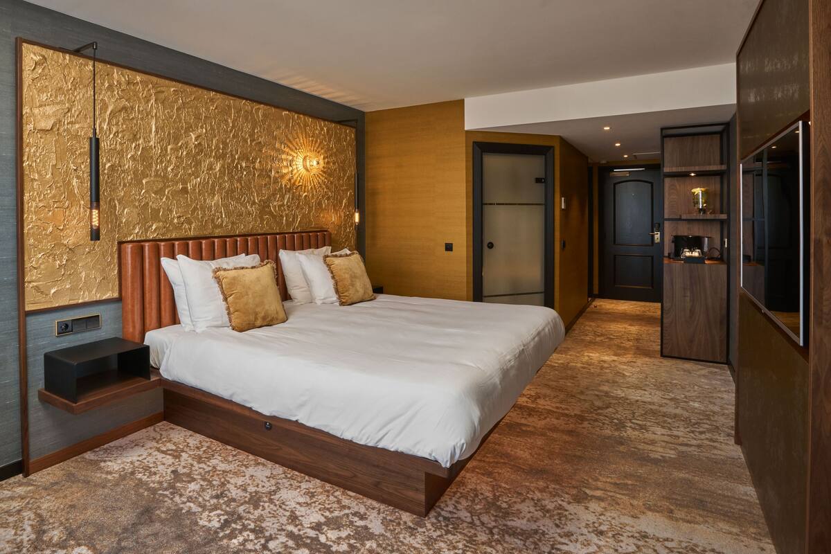 Une chambre moderne avec un grand lit, une table de chevet, une lampe fixée au mur et une armoire en bois.