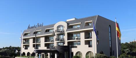 A multi-story hotel with balconies, a flag, and a sign reading "Alexander Hotel."