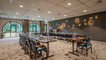 Un salón de conferencias con mesas redondas, sillas y una pared decorativa con detalles dorados.