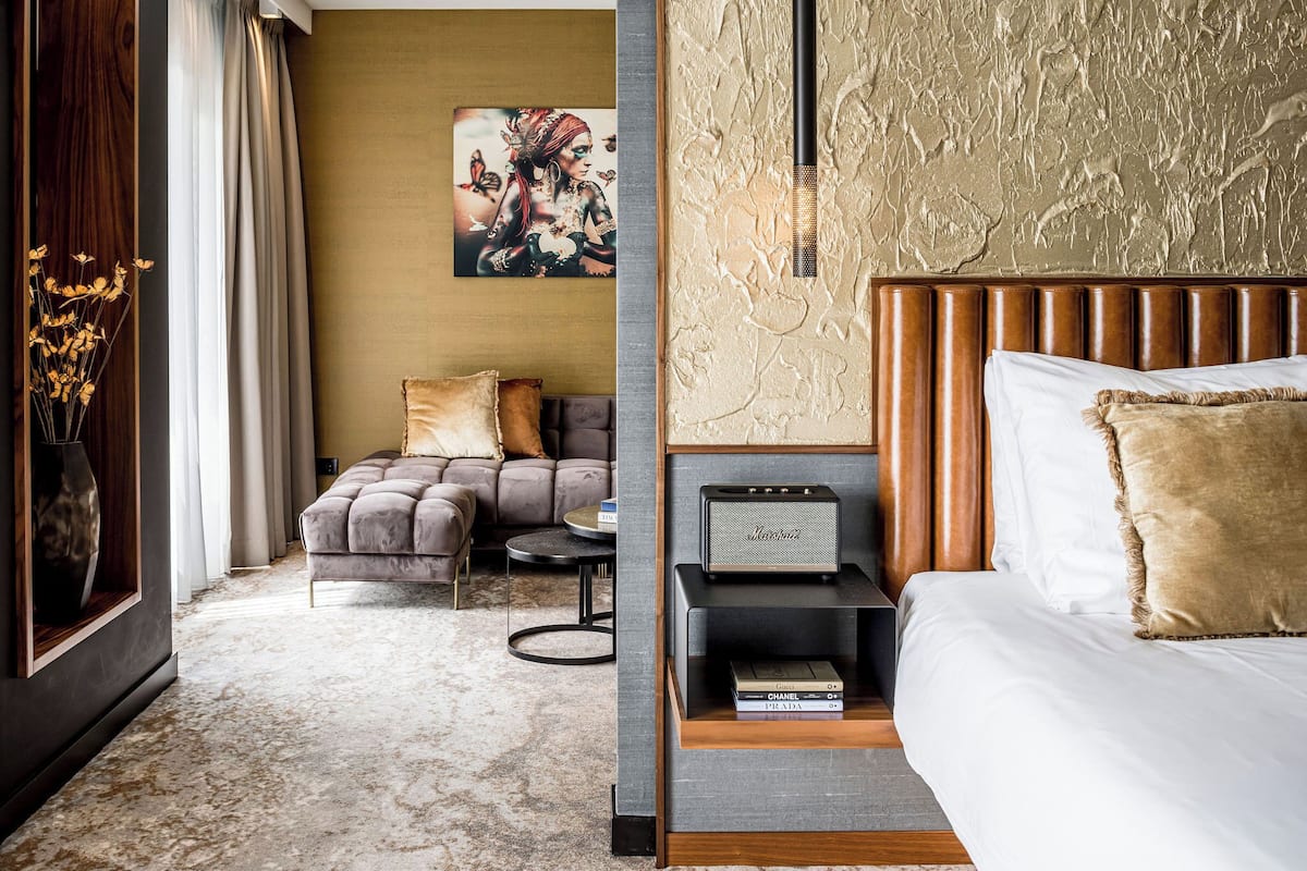 Une chambre d’hôtel moderne avec un grand lit, un canapé, une petite table et un haut-parleur fixé au mur.