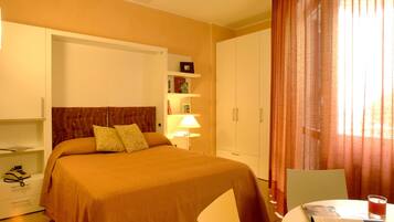 Une chambre d’hôtel comprenant un lit, un bureau avec une chaise, une lampe, une bibliothèque et une armoire.