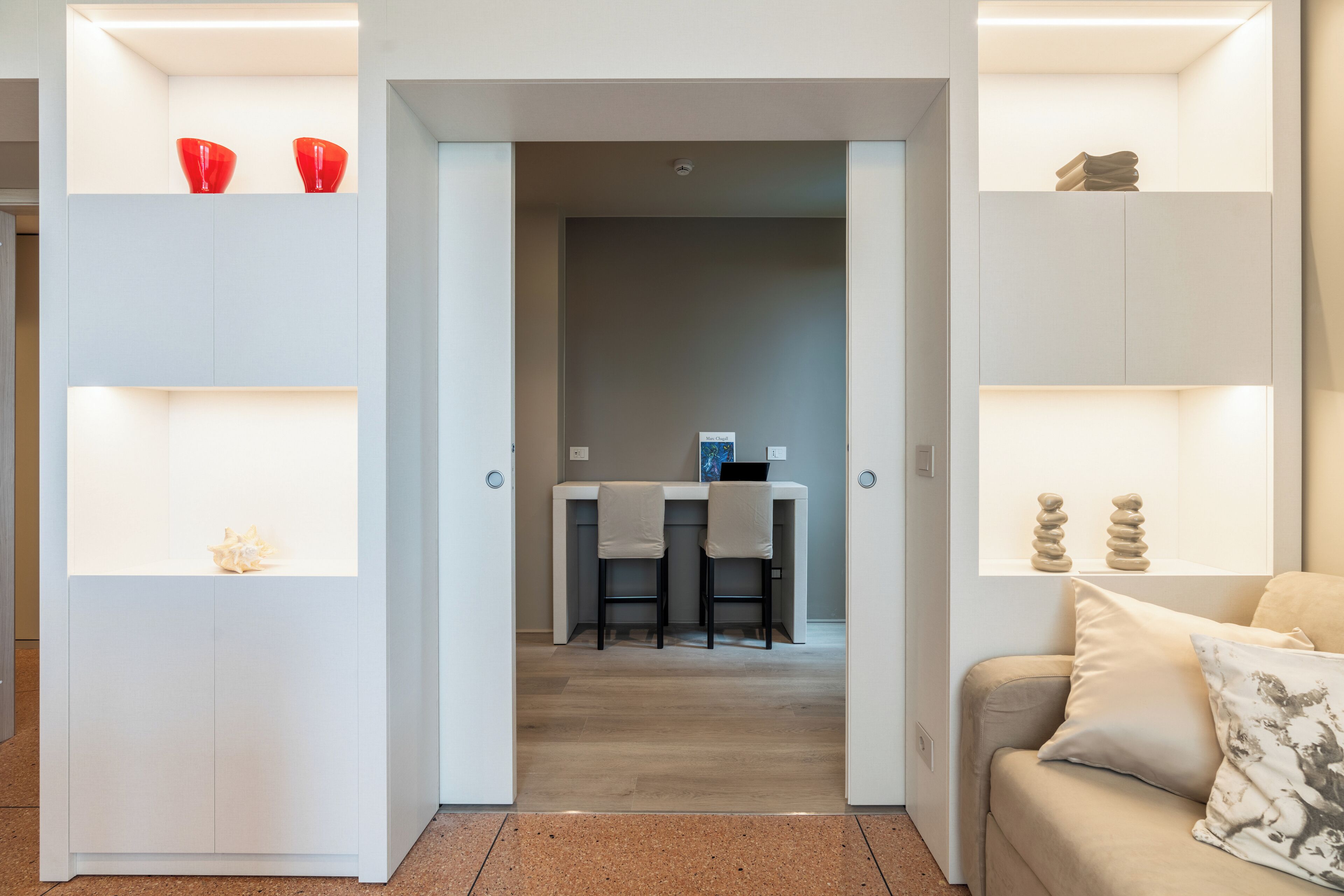A modern interior with a central dining area, a sofa with cushions, and shelves with decorative items.