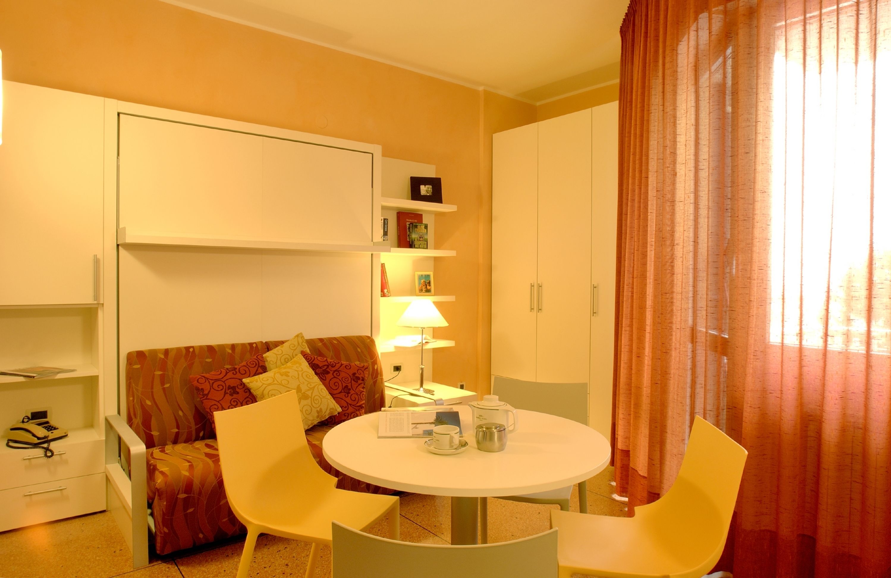 Ein kompakter Raum mit einem runden Esstisch, zwei Stühlen, einer Couch, einem kleinen Schrank und einer Lampe.