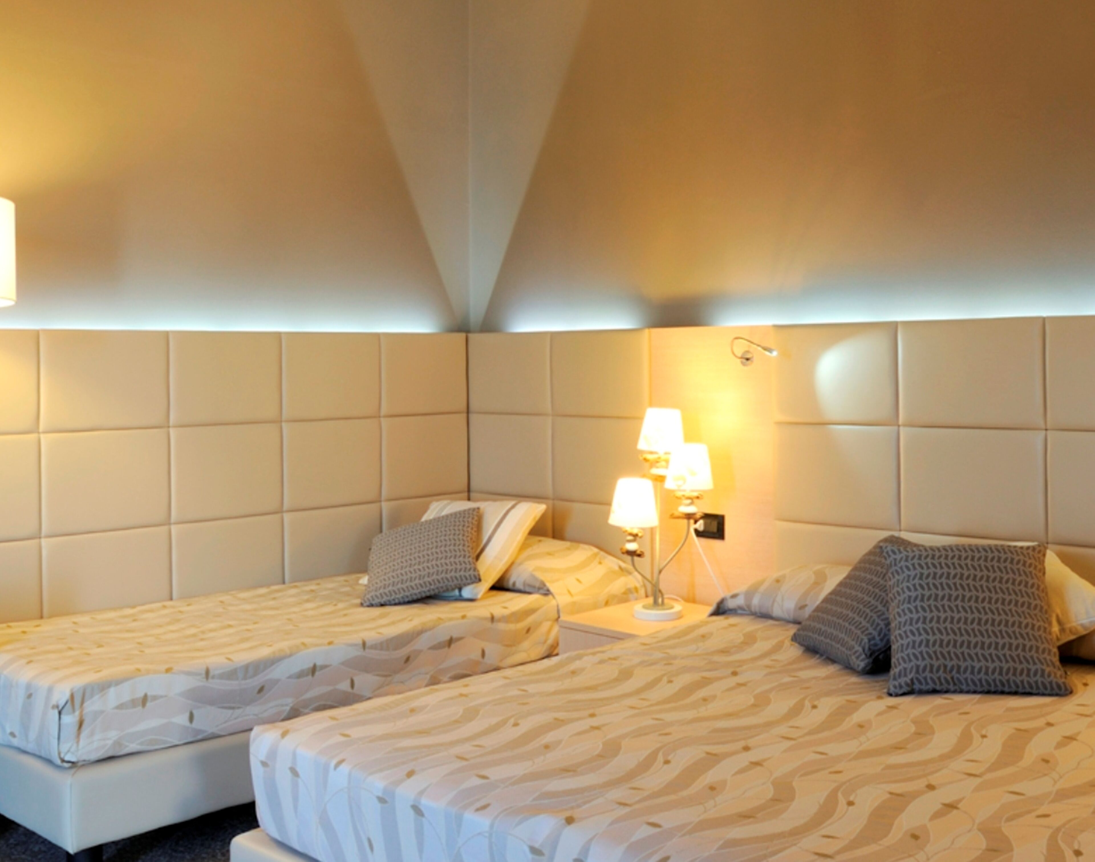 Een hotelkamer met twee bedden, een hoofdeinde, een nachtkastje met lampen en een wandlamp.