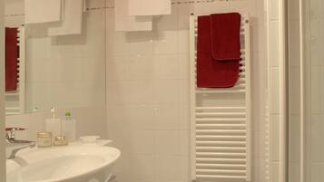 Une salle de bain avec un lavabo blanc, un bidet et une douche. Des serviettes sont accrochées au mur et une serviette rouge est posée sur la tringle de la douche.