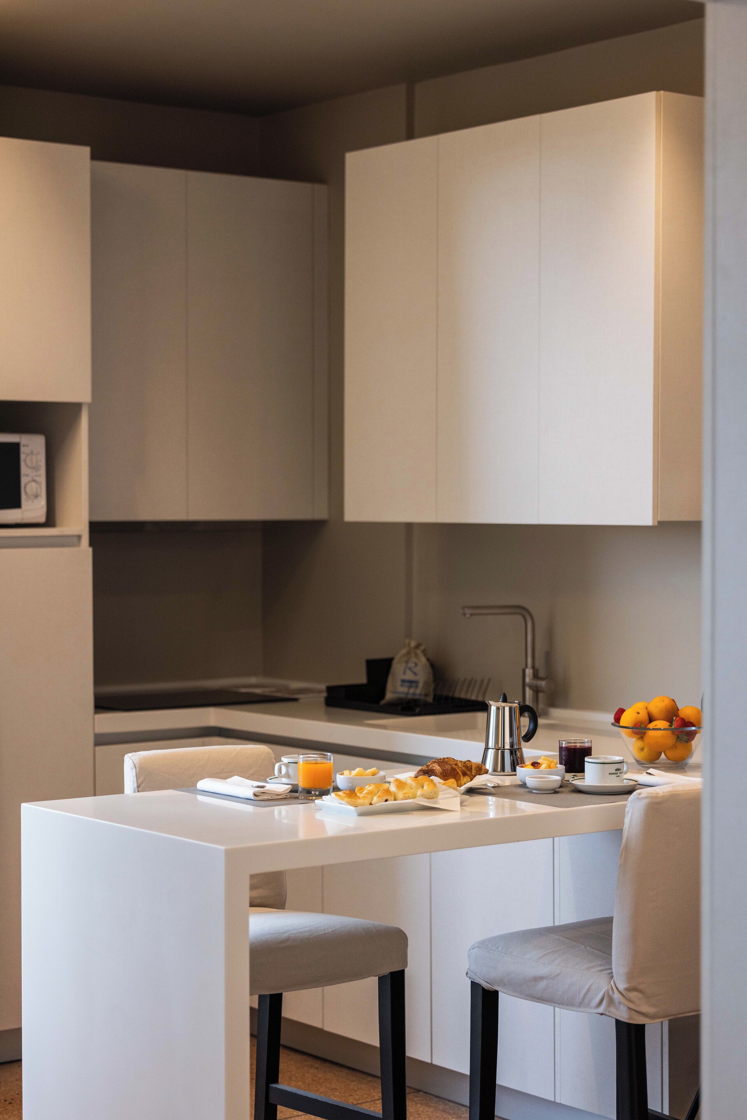 A modern kitchen with white cabinetry, a central island with seating, a microwave, and a fruit bowl.