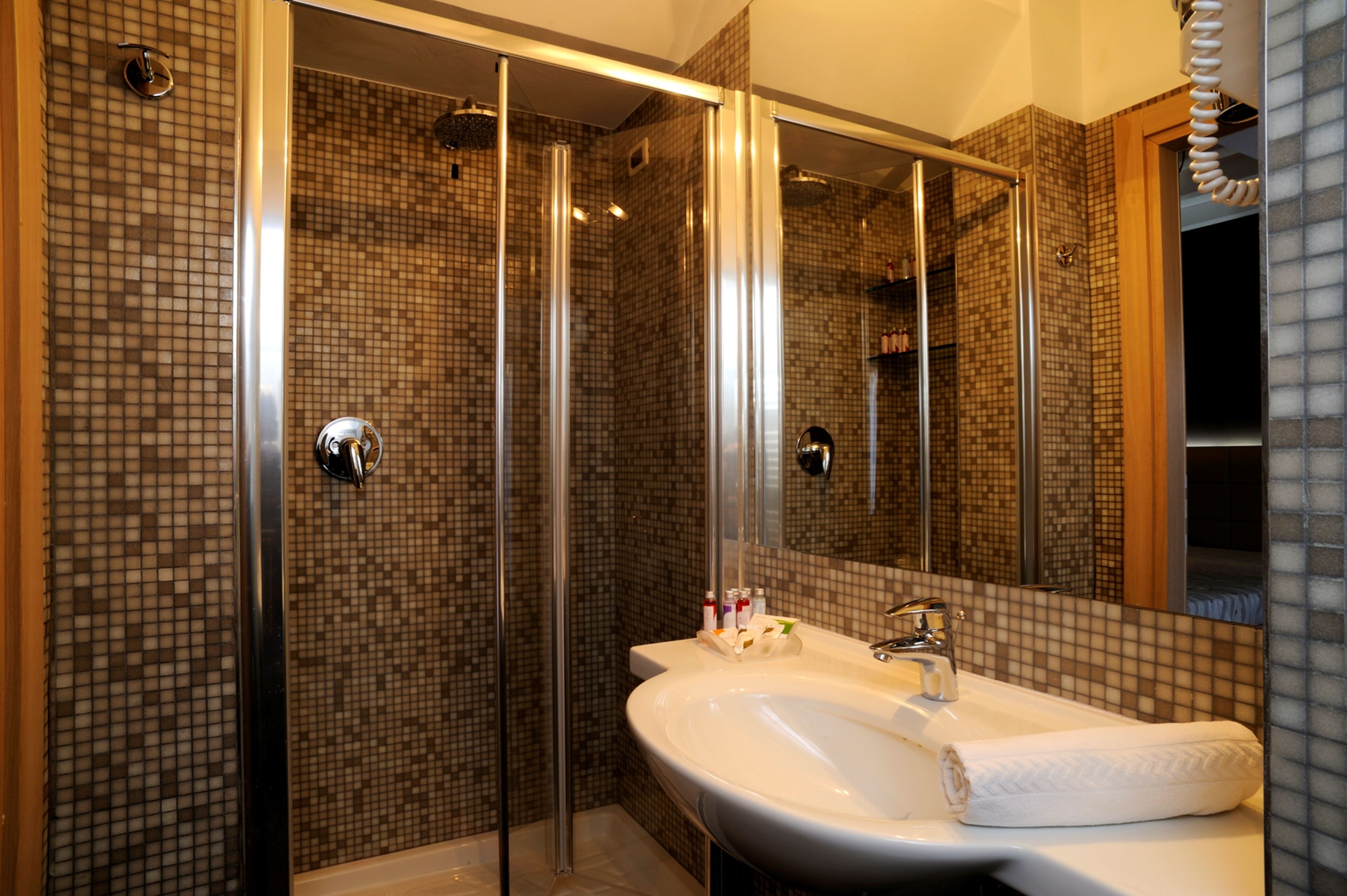 A bathroom with a glass-enclosed shower, a sink with a mirror, and tiled walls.