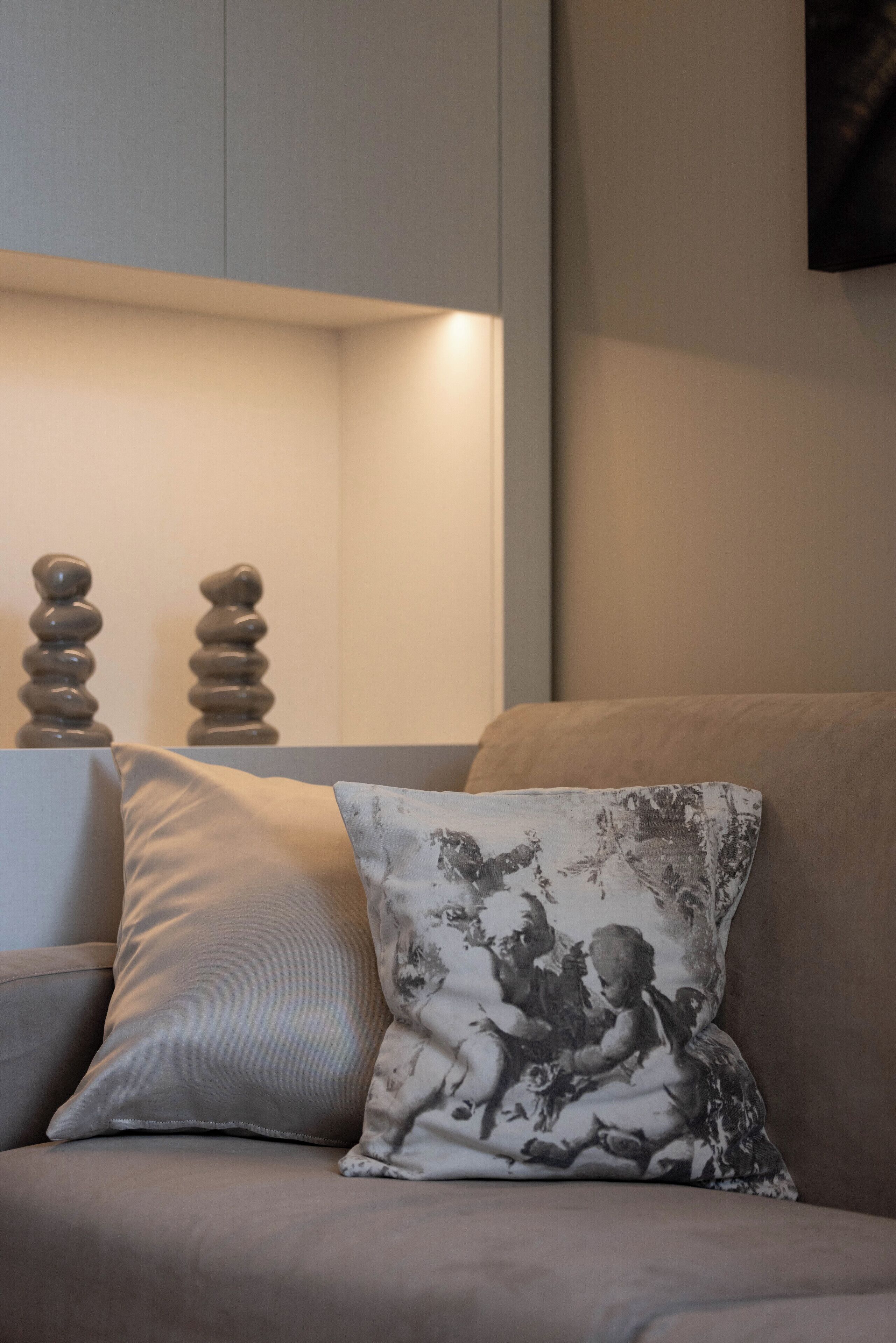 A modern living room with a sofa, a decorative pillow with a classical design, and a wall-mounted lamp.