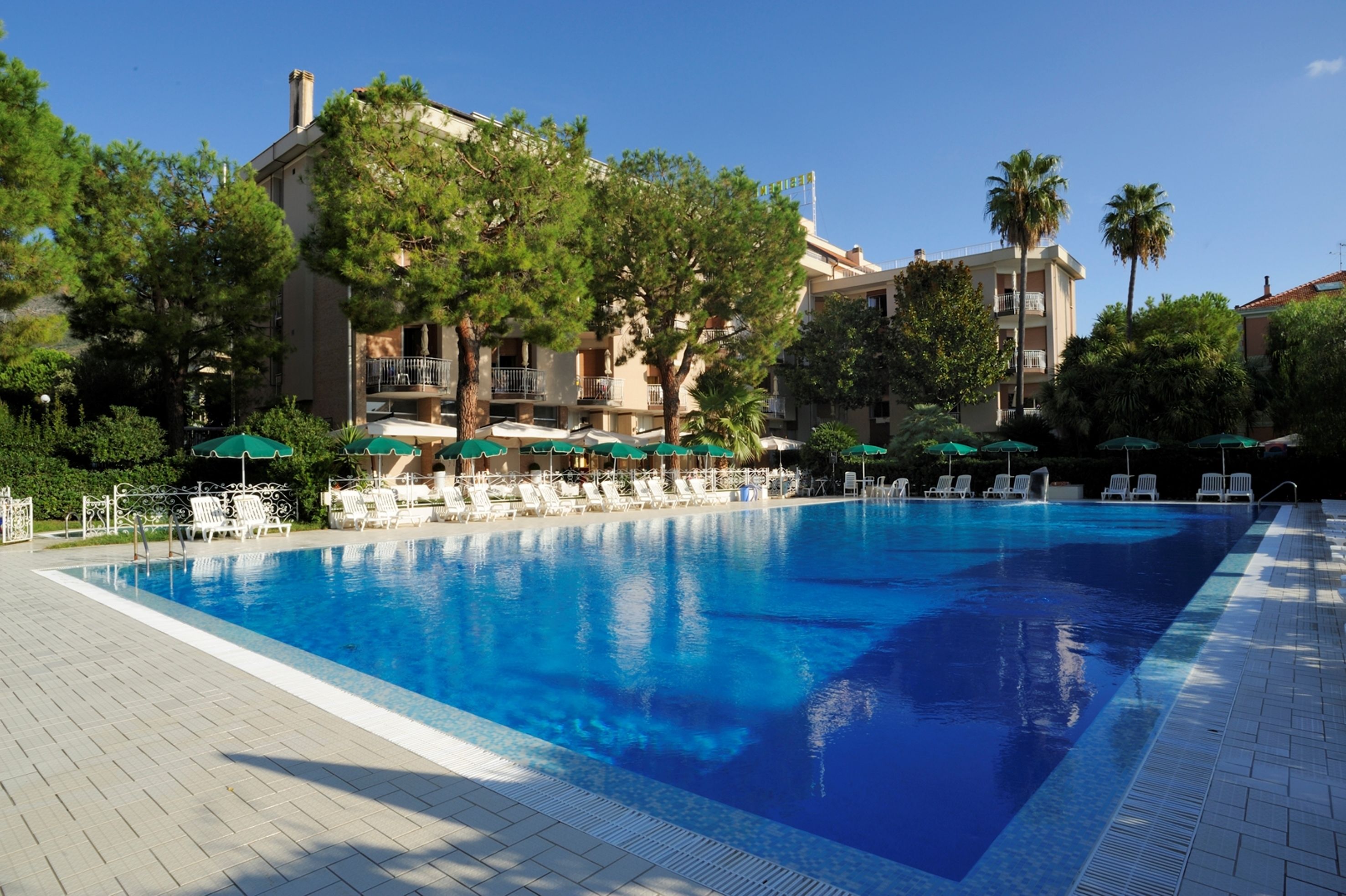 Una piscina amb gandules i ombrelles, envoltada d'arbres i edificis.