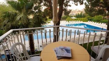 Un espace aménagé au bord de la piscine, avec une table recouverte d’une nappe jaune, des chaises longues blanches et une vue sur la piscine et la plage.