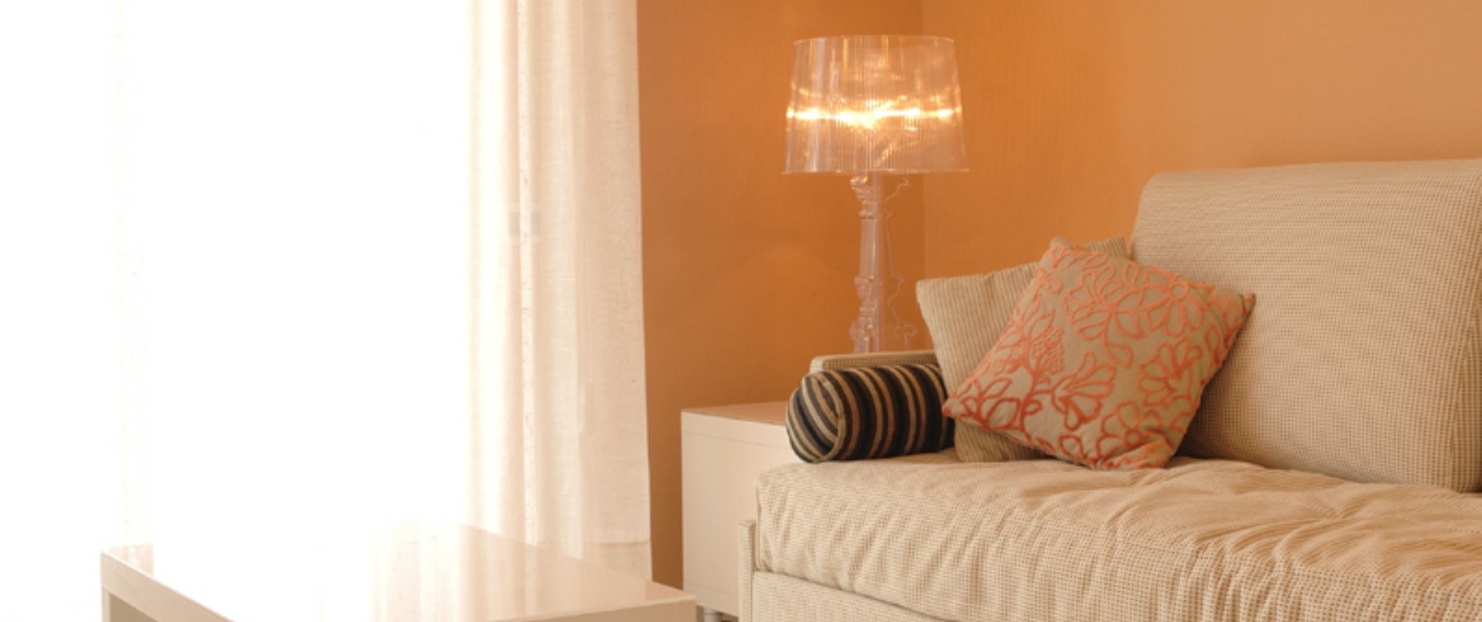 Una habitación con un sofá blanco, un cojín a rayas, un cojín estampado y una lámpara de pie.
