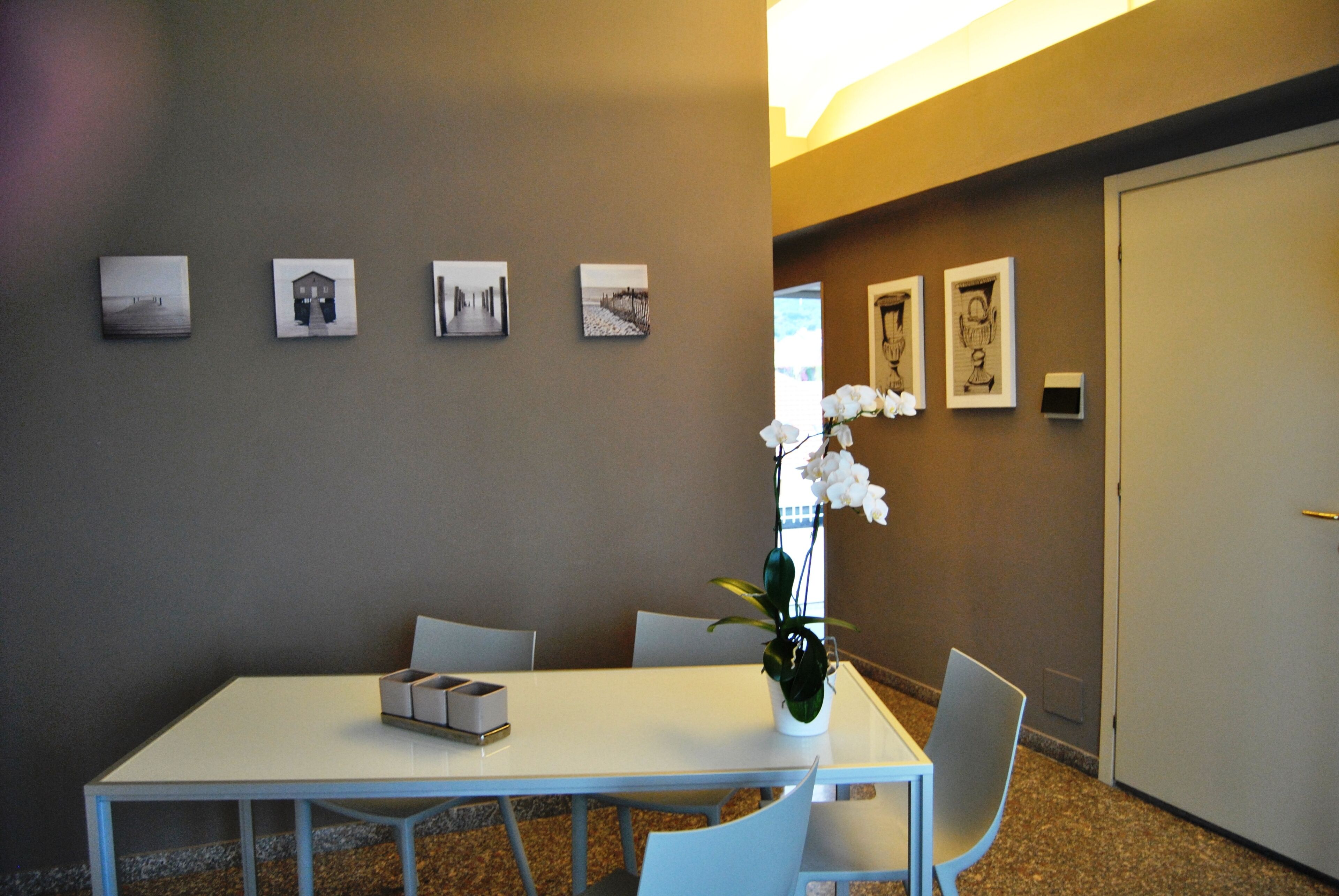 A conference room with a white table, four chairs, a vase with white flowers, and four framed pictures on the wall.