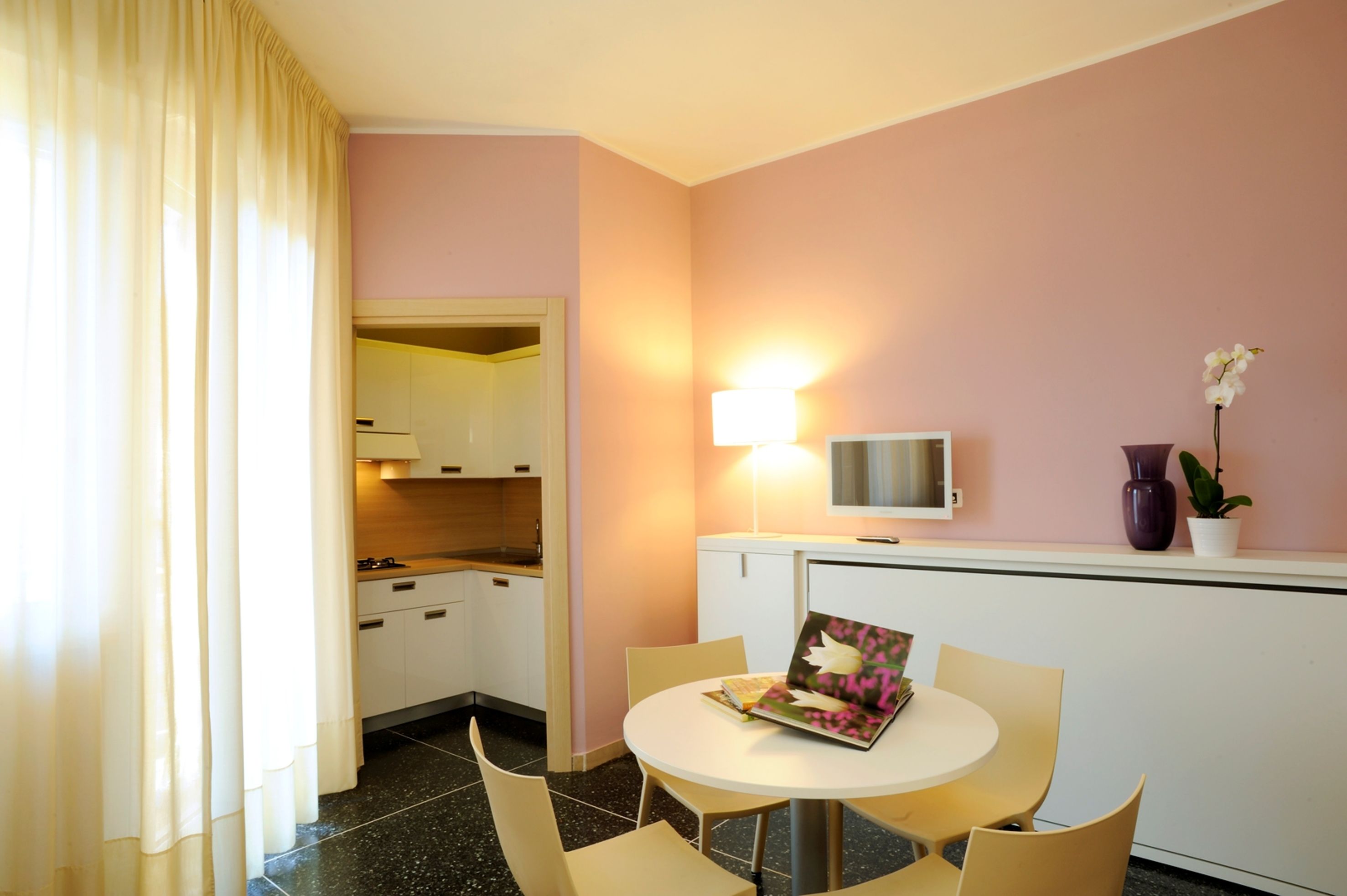 A compact kitchen with white cabinets, a dining area with a round table and chairs, and a small potted plant on the counter.