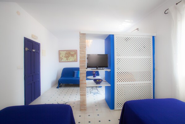 Una habitación con dos camas, televisión, sofá y una mesita con un bol.