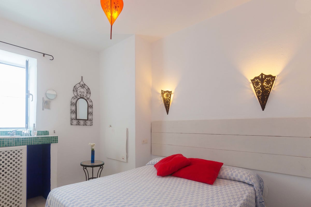 A bedroom with a bed, a nightstand, a mirror, and wall-mounted lights.