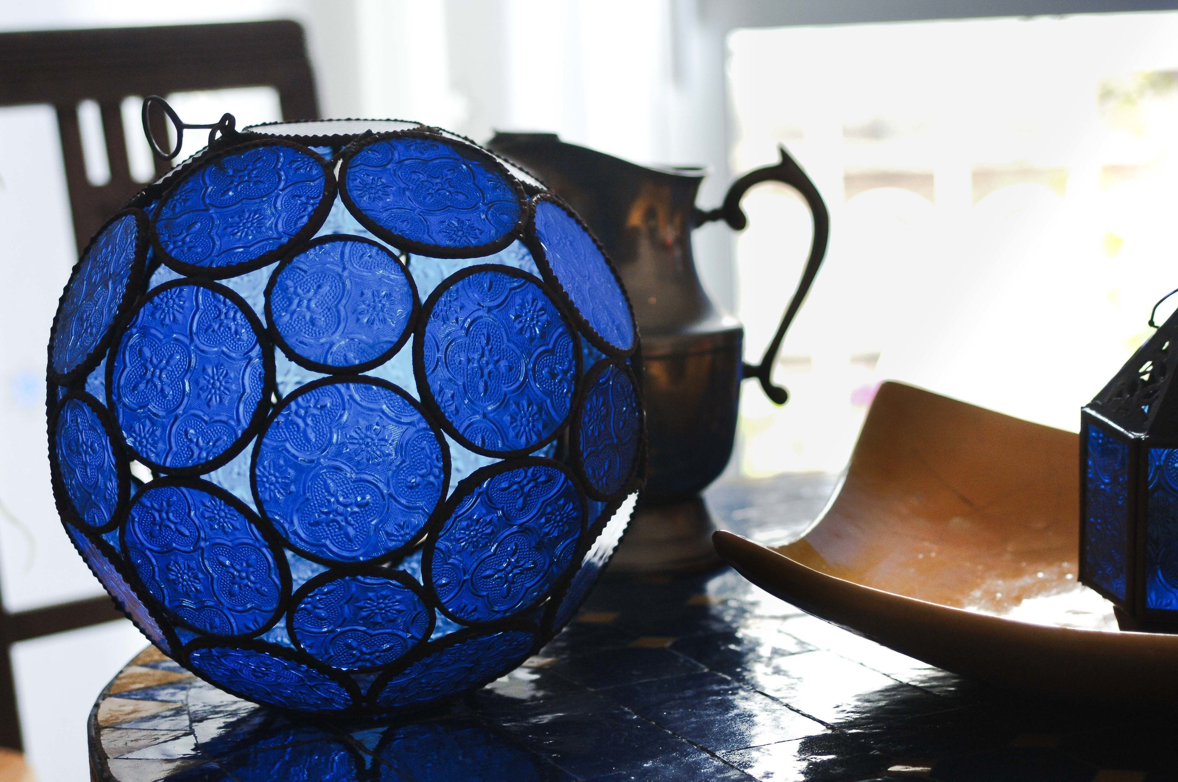 Eine blaue Glaskugel mit strukturierter Oberfläche, eine Kupferkanne und eine kleine, blaue Schachtel auf einer spiegelnden Fläche.