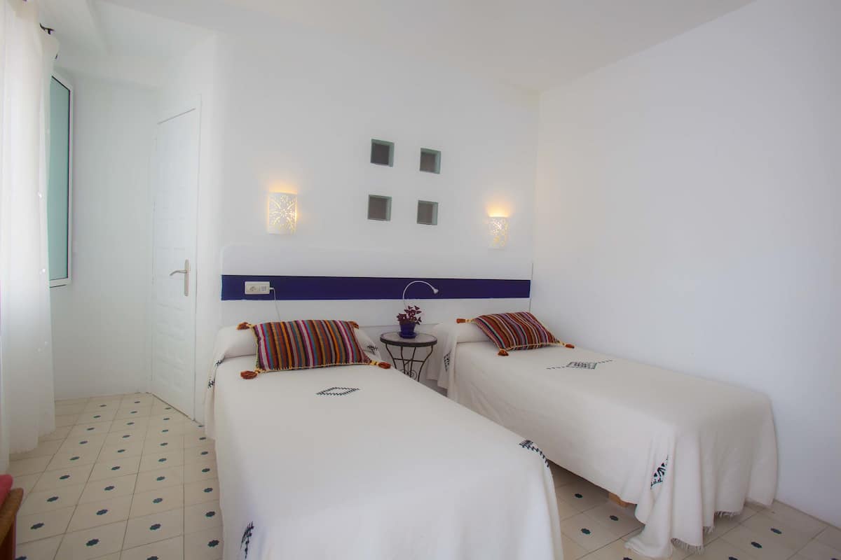 A hotel room with two beds, a small table, and a wall-mounted light fixture.