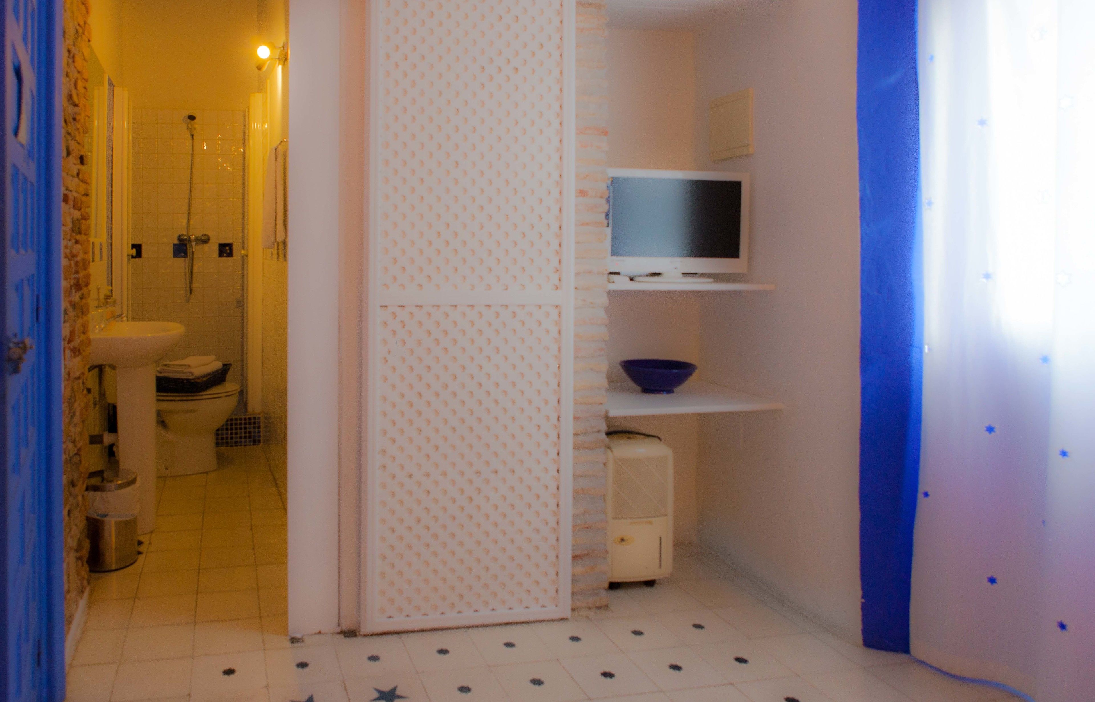 Casa de banho compacta com sanita, lavatório, chuveiro e uma televisão num armário.