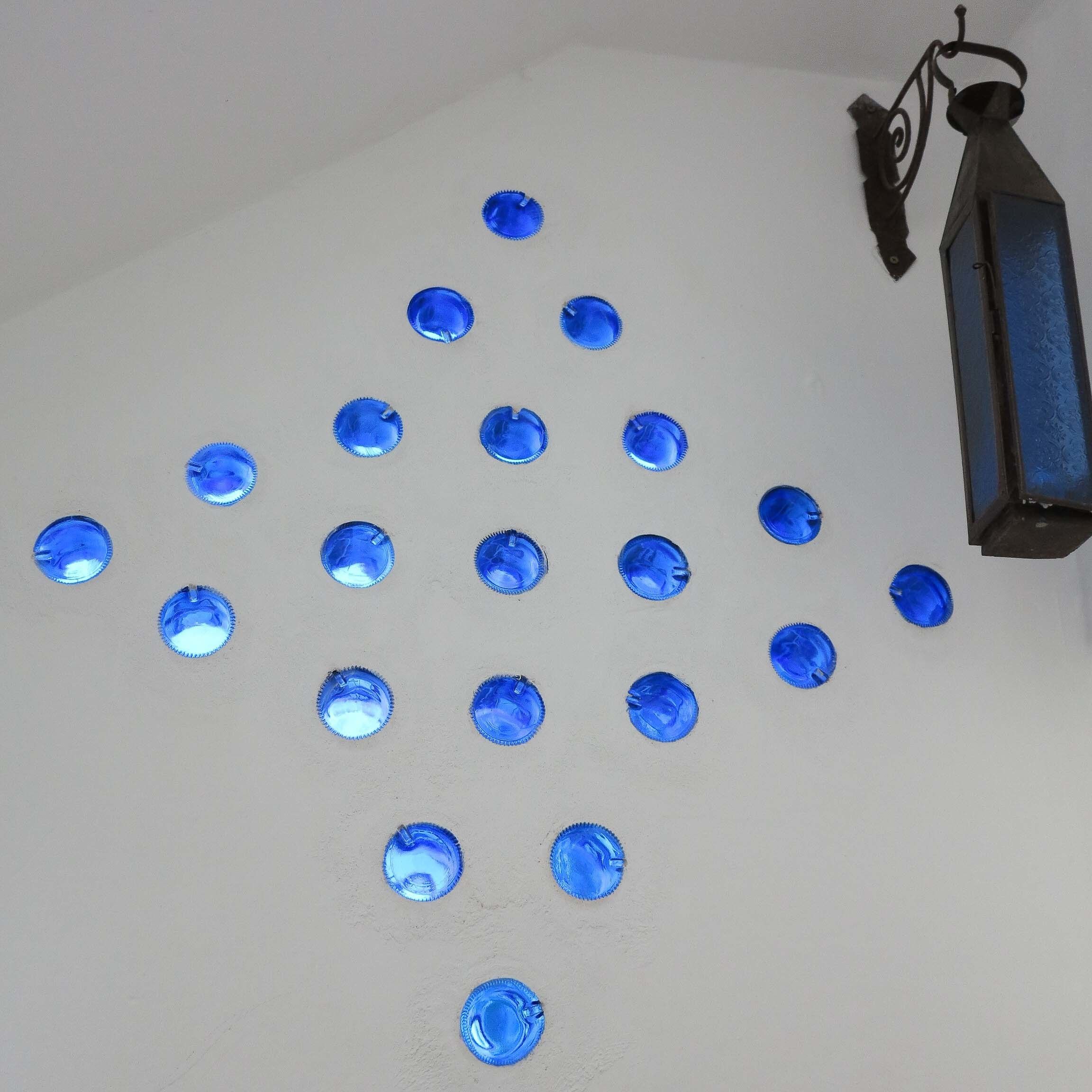 A ceiling with blue bottle caps arranged in a pattern and a black lantern hanging on the right.