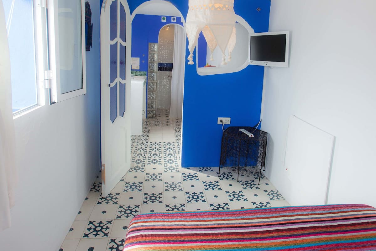 A narrow hallway with a bed at the end, a shower area, and a TV mounted on the wall.