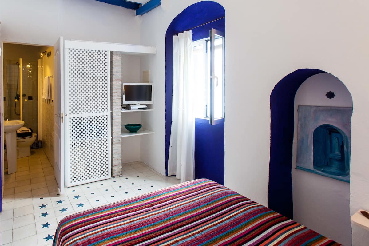 A bedroom with a bed, a TV, a bathroom with a shower, and a blue arched doorway.