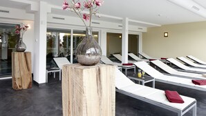 A spa area with wooden stools, a large vase with pink flowers, and sun loungers. - NaturKulturHotel Stumpf (Neunkirchen)