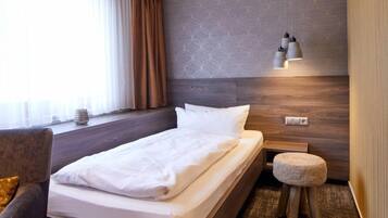 Una habitación de hotel moderna con una cama de madera, un pequeño reposapiés, una mesita de noche y una pared con estampado.