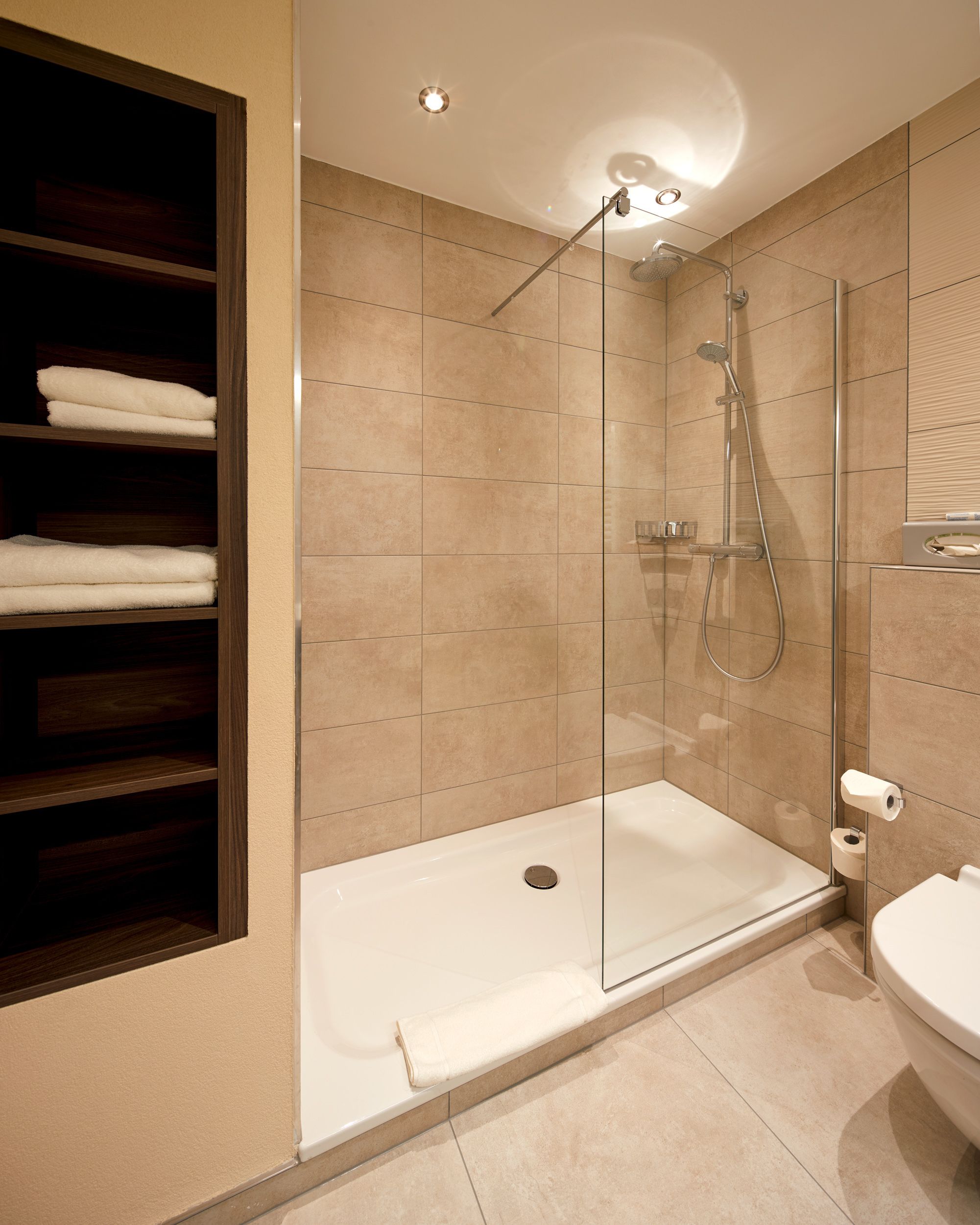 A modern bathroom with a glass shower enclosure, a white bathtub, and a wooden shelf with towels.