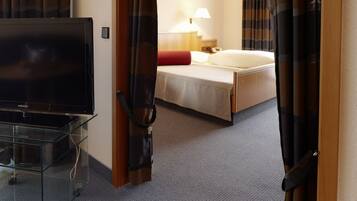A hotel room with a bed, a TV on a glass stand, a lamp, and a door with curtains.