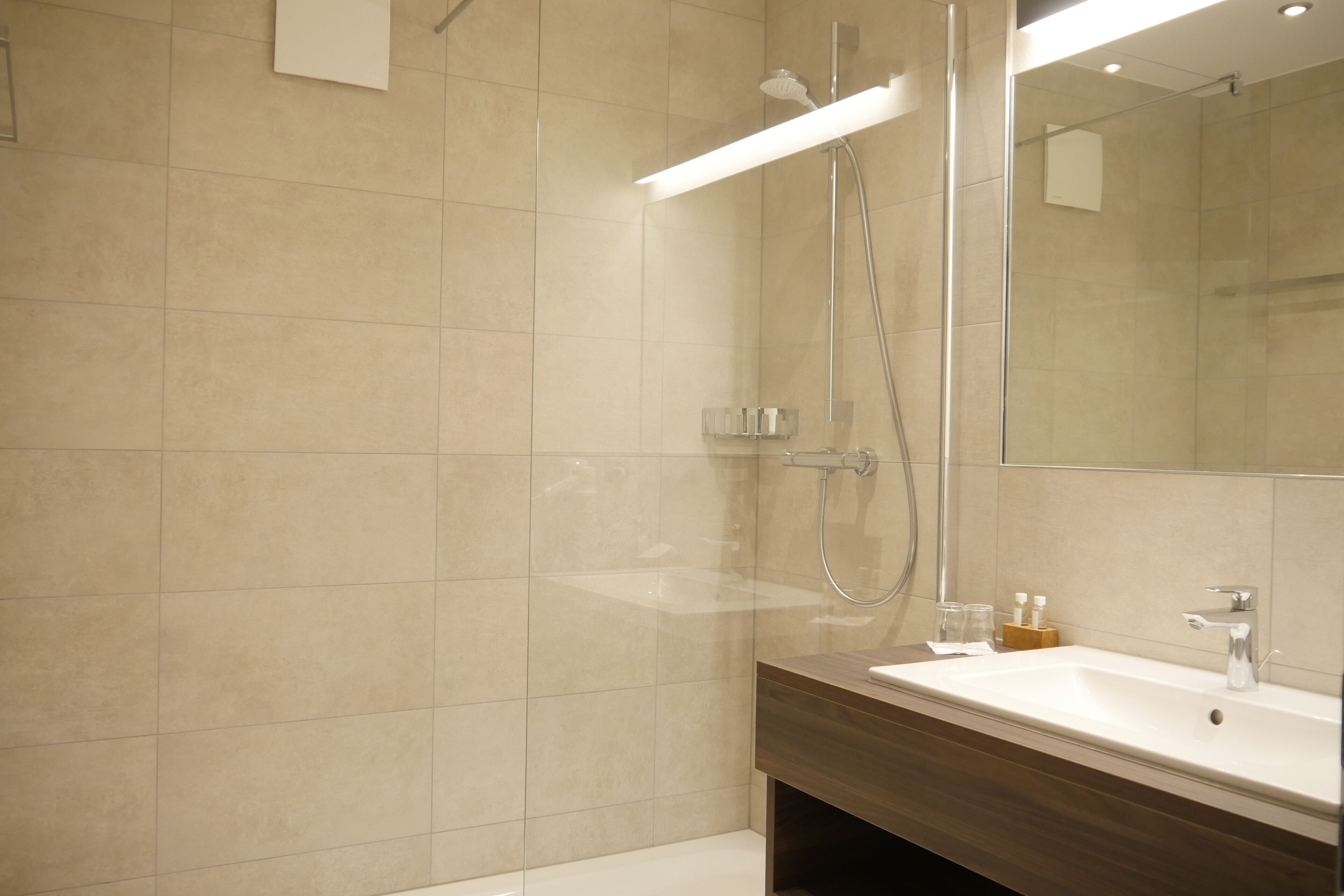 Une salle de bain moderne avec un grand miroir, une douche et un lavabo.