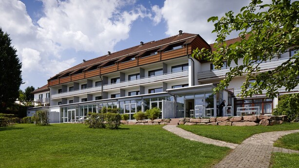 A multi-story hotel with a modern design, featuring a glass facade, a brick roof, and a well-maintained lawn. - NaturKulturHotel Stumpf (Neunkirchen)