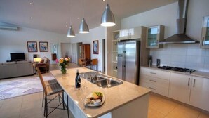 A modern kitchen with a central island, stainless steel appliances, pendant lighting, and a dining area with a sofa and table.