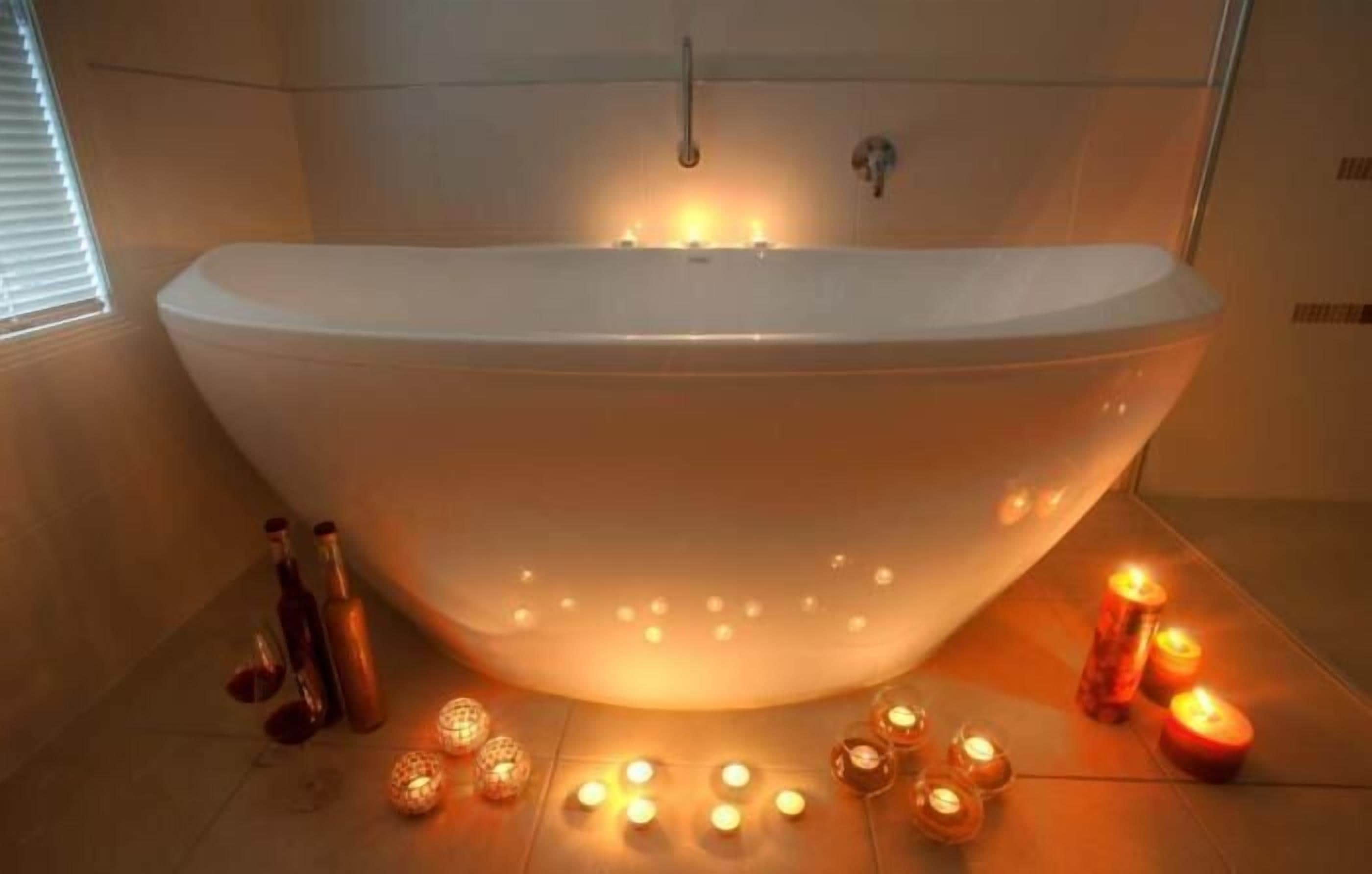 Un baño moderno con una bañera independiente, velas y botellas en el suelo.
