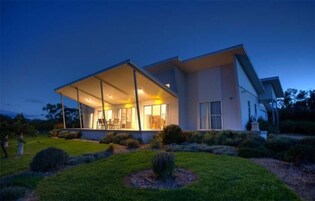 A modern house with a large covered patio, a well-maintained lawn, and a clear sky.