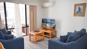 Una sala de estar con dos sofás, una mesa de centro, un televisor y un balcón con una silla.