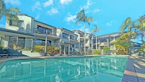 Una piscina con superficie de agua azul cristalina, rodeada por un edificio de varios pisos con balcones y palmeras.