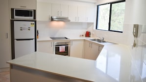 Una cocina moderna con armarios blancos, una campana extractora de acero inoxidable, un microondas, un horno empotrado y un ventanal que proporciona luz natural.