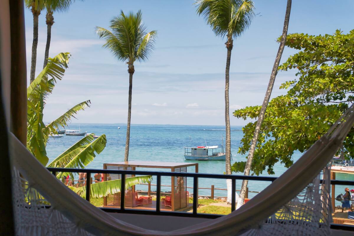 A hammock overlooking a beach with palm trees and a boat in the water.