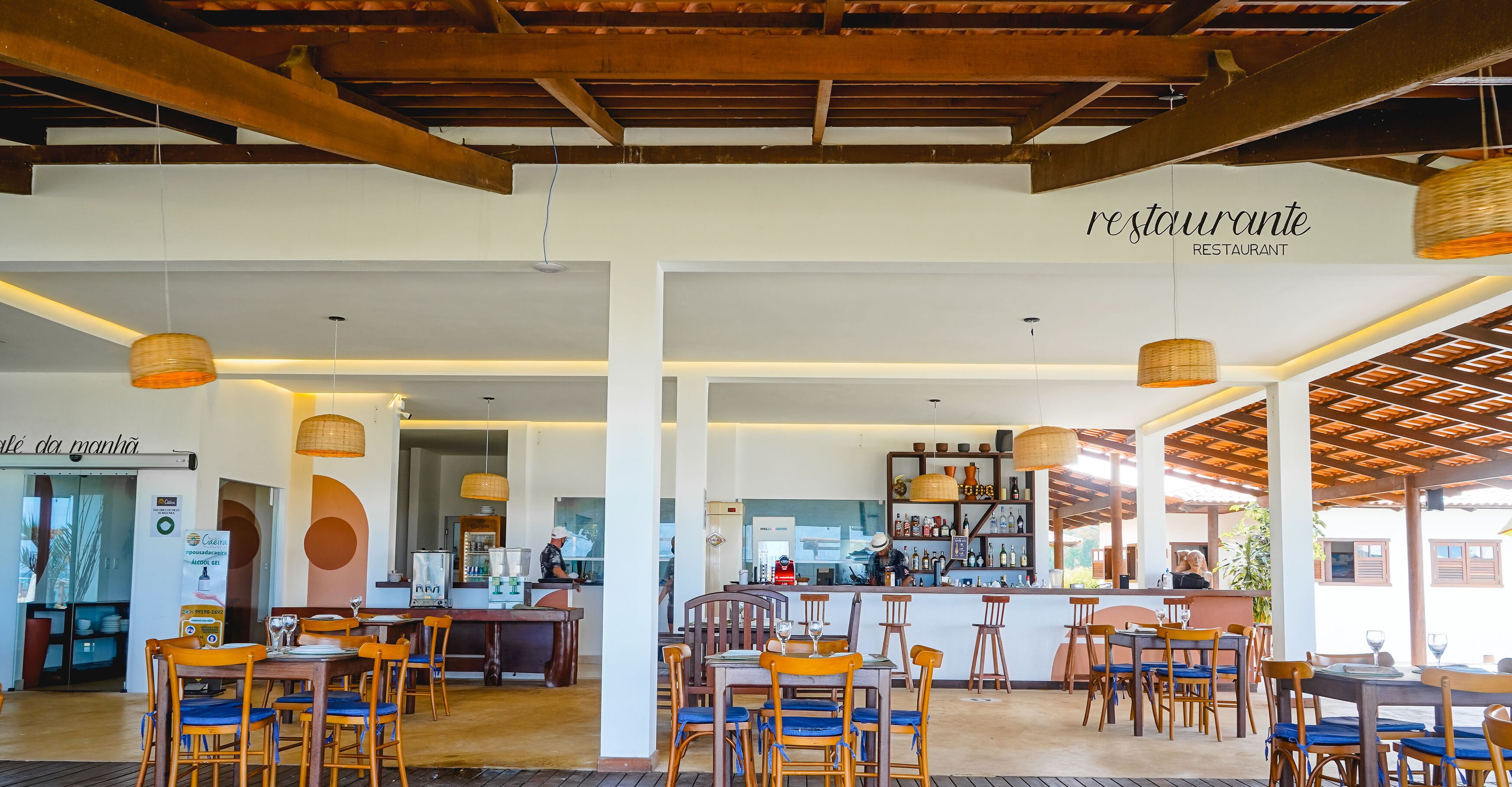 A restaurant with wooden beams, hanging wicker lamps, and a bar area.