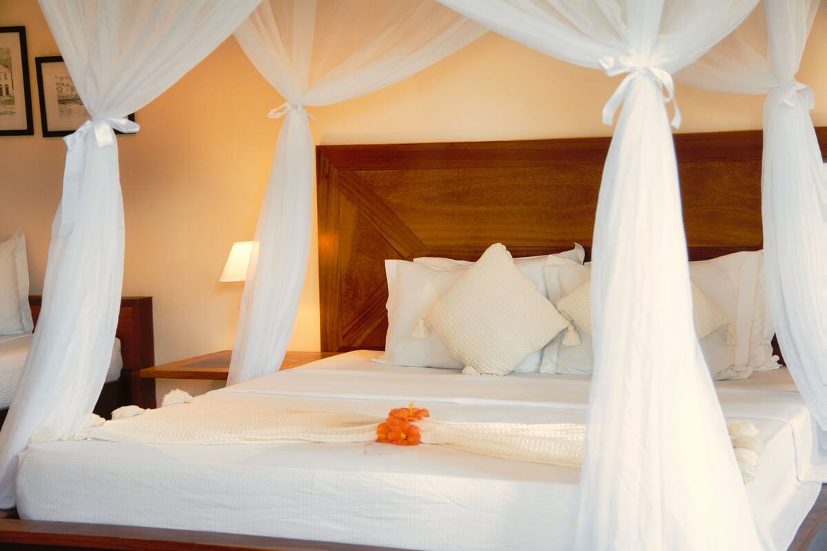 A hotel room with a four-poster bed, white bedding, and a nightstand with a lamp.